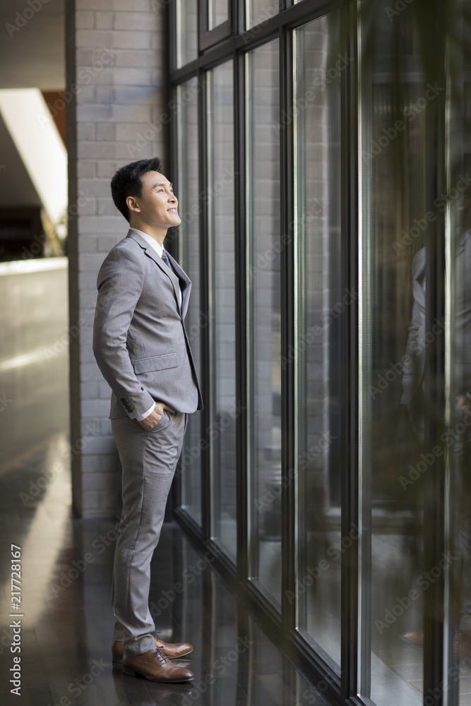 Confident businessman looking through window Confident businessman looking through window