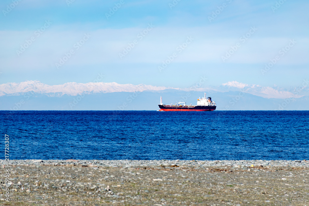 Cargo ship in open sea against the background of snow covered mountains. View from the shore. Georgia, Batumi.