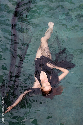 Fashion photo of woman wrapped in black sheer fabric in swimming pool
