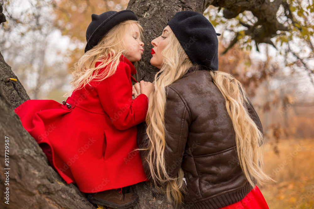 Fototapeta premium girl in a red coat climbed up an old tree and her mother supports
