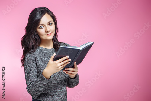 Attractive young woman holding notebook on pink background.