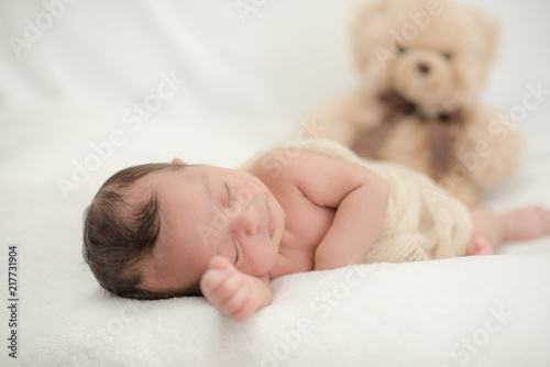 Cute newborn baby sleeps on a blanket with a toy teddy bear - happy family moments