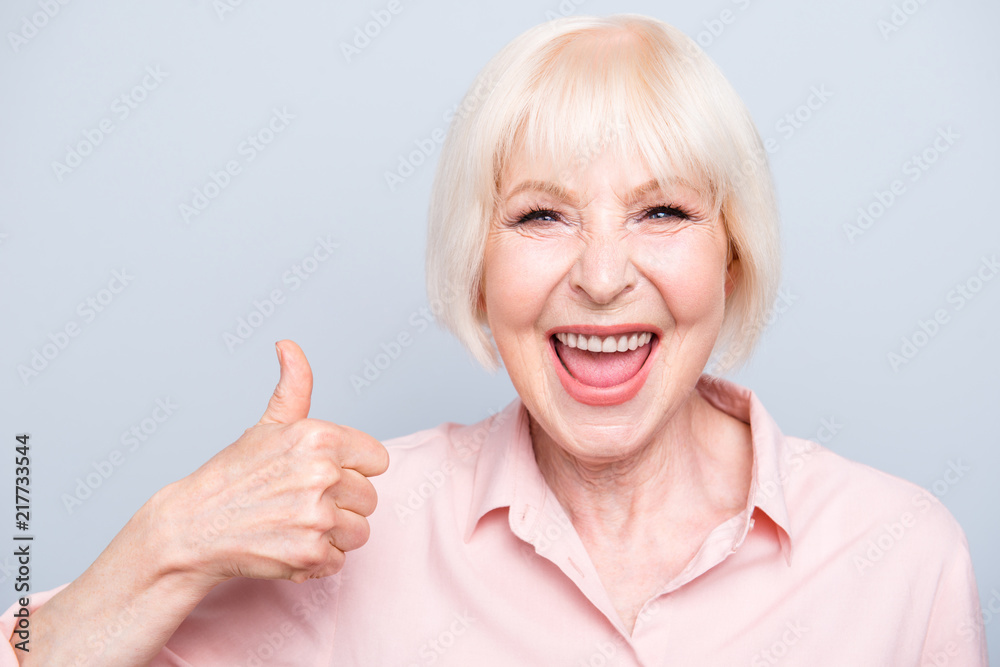 Old excited lady showing thumbs up gesture, laughing on grey bac Old excited lady showing thumbs up gesture, laughing on grey bac
