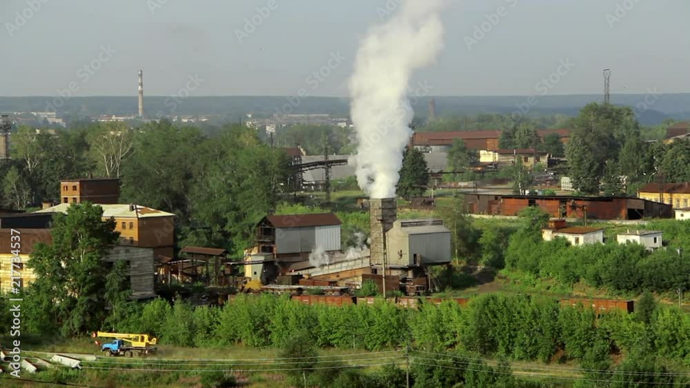 Pipes of industrial plant smoke among green trees and nature in