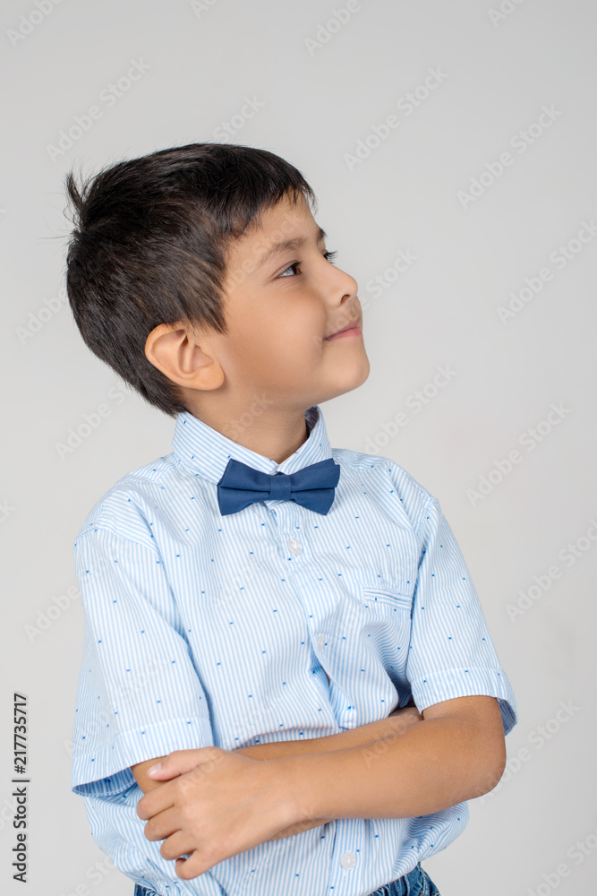 Portrait of smiling boy wearing; blue shirt with tie- bow with arm crossed; on a gray background in the studio Portrait of smiling boy wearing; blue shirt with tie- bow with arm crossed; on a gray background in the studio