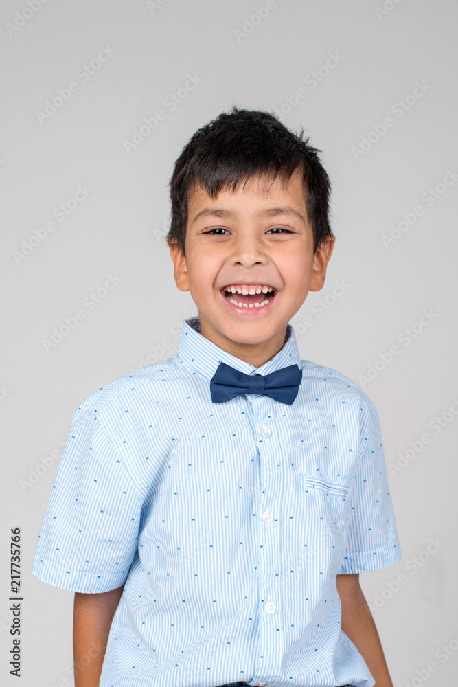 Waist up emotional portrait of smiling boy wearing blue shirt with tie-bow on a gray background in the studio Waist up emotional portrait of smiling boy wearing blue shirt with tie-bow on a gray background in the studio