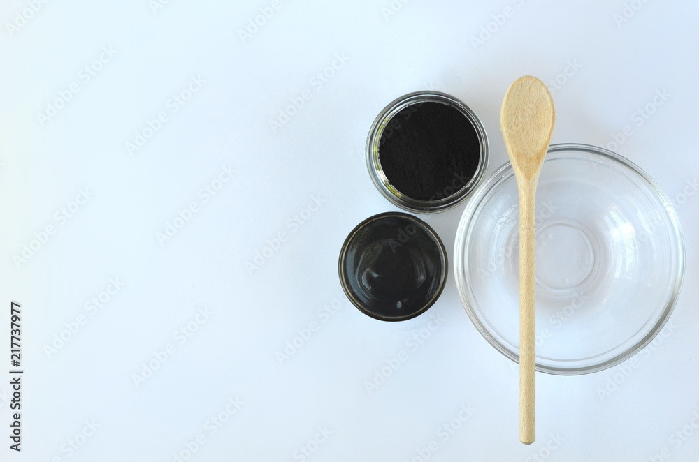 Top view of cosmetic black powdered activated charcoal and beauty face mask mixture in a bowl with copy space on white. 
