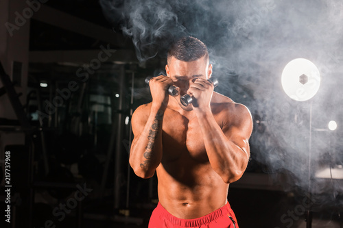 Powerful man doing boxing exercises, making direct hit with dumbbells. Photo of sporty muscular male. Strength and motivation photo