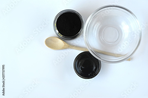 Top view of cosmetic black powdered activated charcoal and beauty face mask mixture in a bowl with copy space on white. 