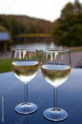 Romantic couple of glasses of wine on a table with reflections and view of nature on background