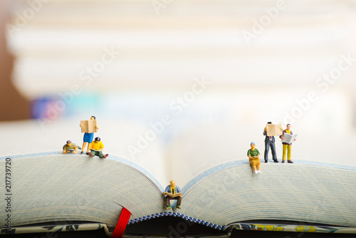 Close up of miniature figures of a group of people read book and newspaper.