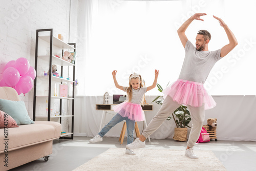 funny father and daughter in pink tutu skirts dancing like ballerinas