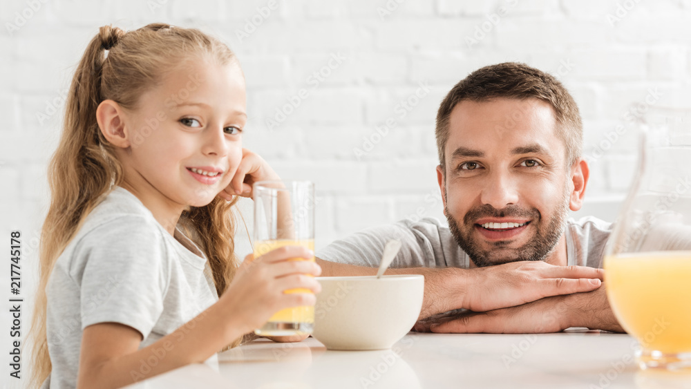 father and daughter drinking orange juice and looking at camera father and daughter drinking orange juice and looking at camera