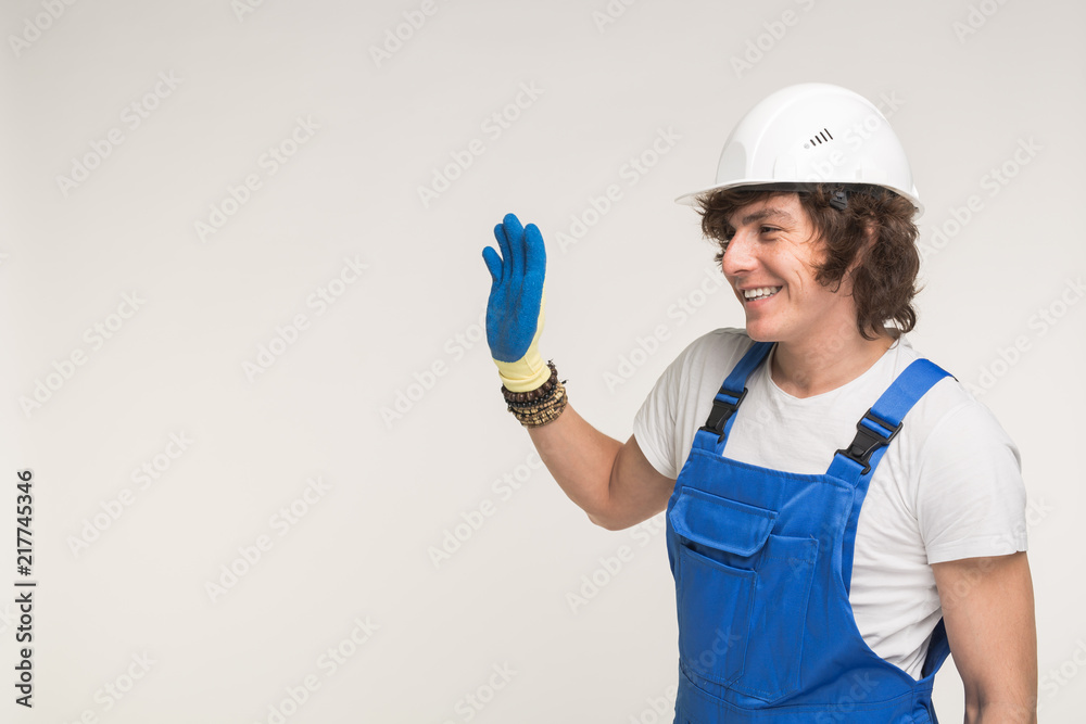 Portrait of handsome builder in white helmet and blue overall shaking his hand and laughing on white background with copy space Portrait of handsome builder in white helmet and blue overall shaking his hand and laughing on white background with copy space