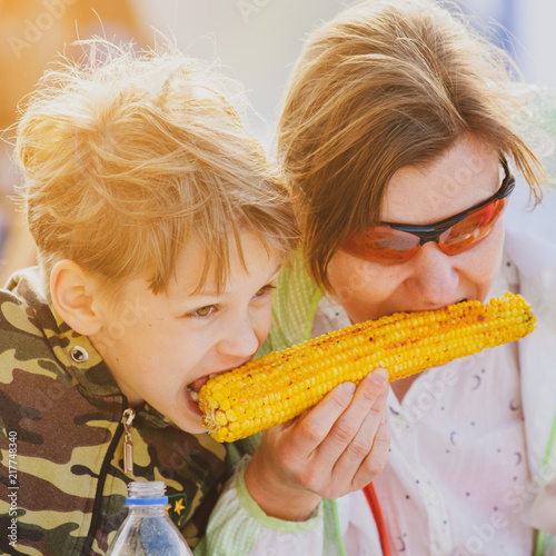Portrait of mother and son eating yellow grilled corn outdoor