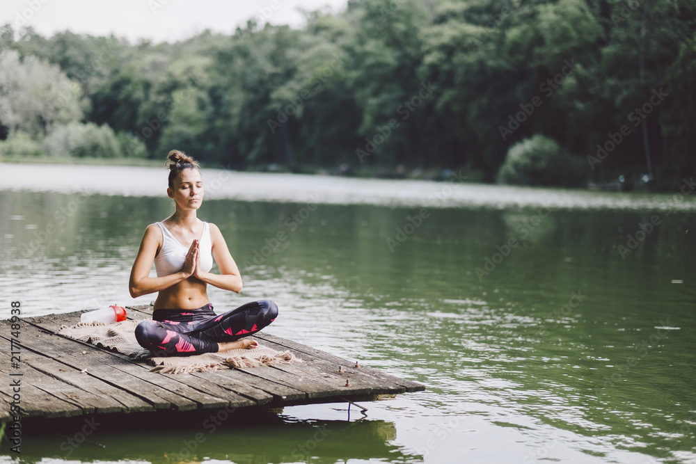 Woman meditating while sitting on pier over lake in forest Woman meditating while sitting on pier over lake in forest