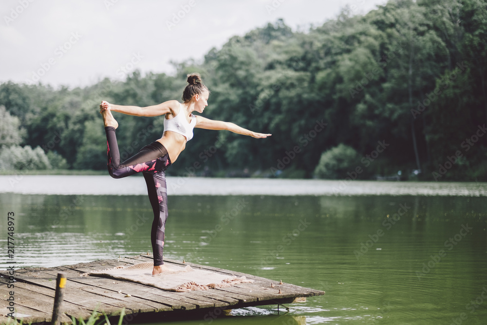 Woman practicing yoga while standing on pier over lake in forest Woman practicing yoga while standing on pier over lake in forest