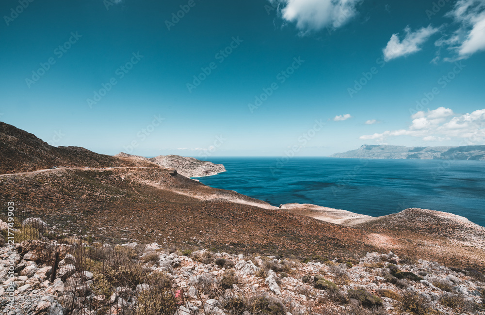 Panoramic view of rocks and beach with sky and clouds in Crete, Greece. Amazing scenery with crystal clear water and the rock formation against a deep blue sky during Summer period. Greece, Europe