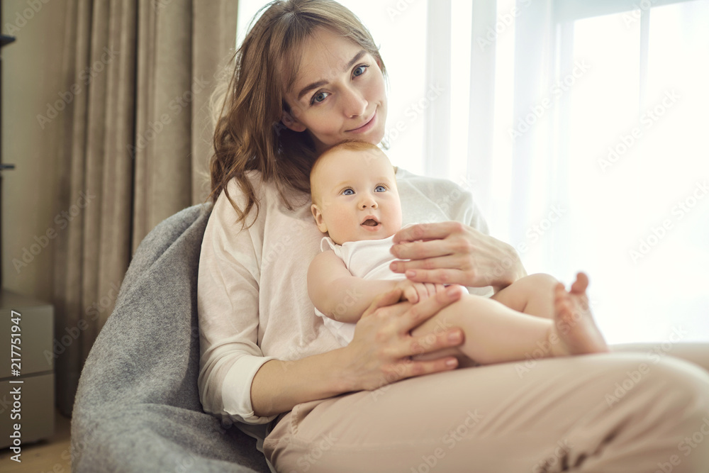A mother with a baby in her arms sitting on a chair in front of a window in the room. A mother with a baby in her arms sitting on a chair in front of a window in the room.