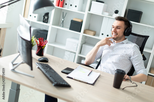 A young man in headphones sits at a computer desk. photo