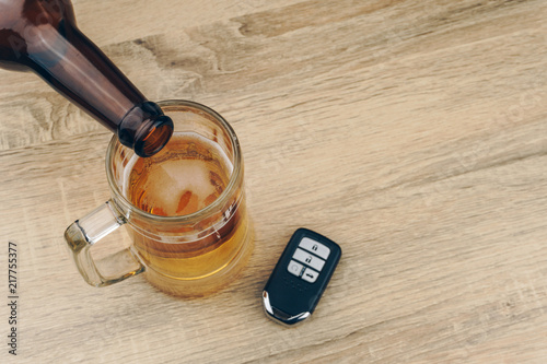 Fototapeta Naklejka Na Ścianę i Meble -  do not drink and drive concept, pouring beer from the bottle into a mug, a remote car key on wooden table