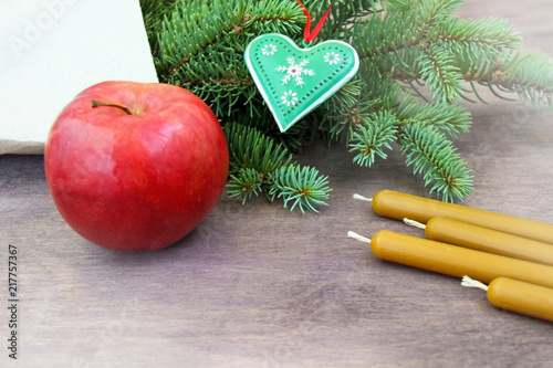 Christmas party preparation background with red apple, natural wax candles near fresh natural branches of Christmas tree spruce decorated with heart and snowflakes on brown natural wooden background.  photo