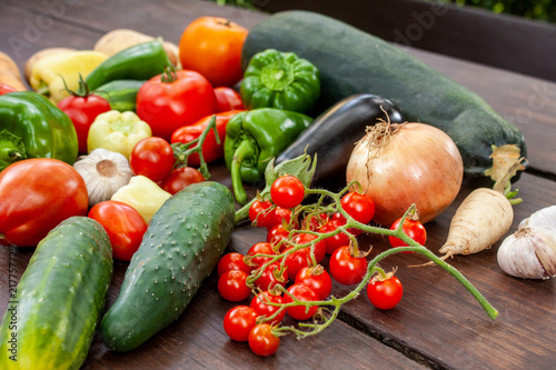 Colourful variety of fresh home grown vegetables from an organic garden on a wooden surface. Tomato, green and yellow bell peppers, carrot, parsley, onion, garlic, potato, eggplant and zucchini.