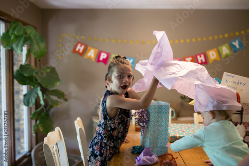 Portrait of surprised girl with sister opening birthday gifts on table at home