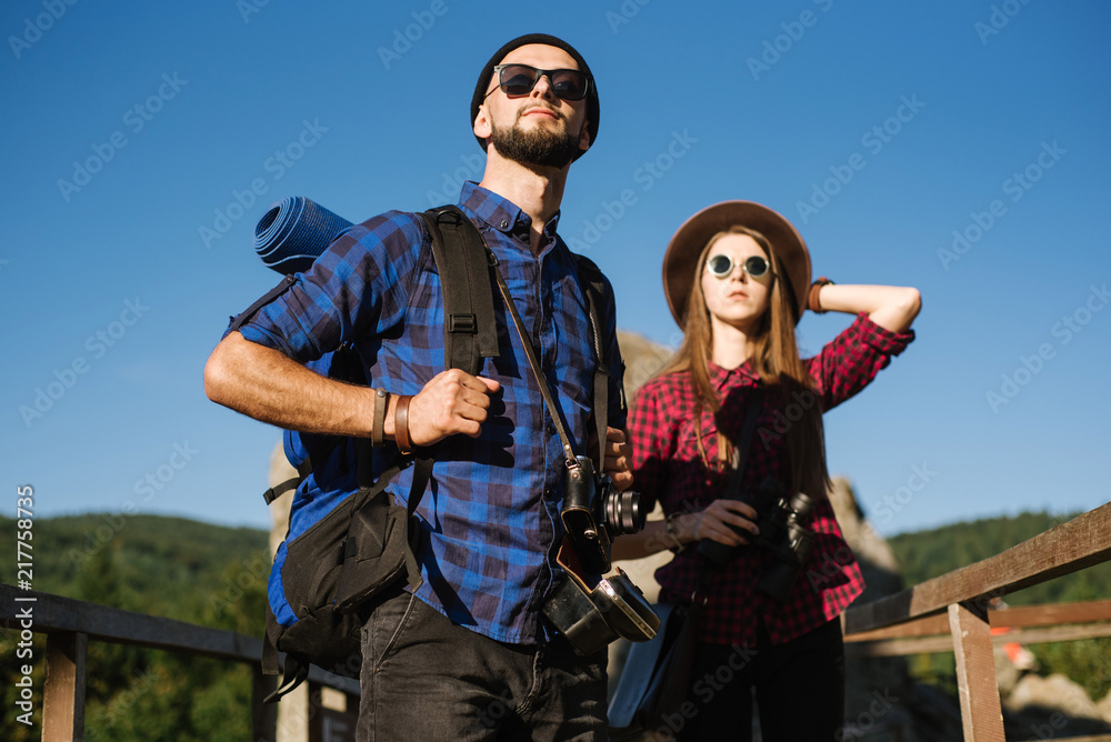 A couple traveling by the mountains wearing hipster clothes with backpack, vintage camera and binoculars