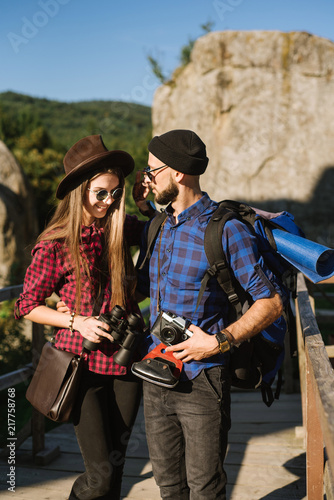 A couple traveling by the mountains wearing hipster clothes with backpack, vintage camera and binoculars