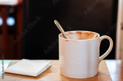 Empty white coffee mug with stained and stainless spoon lay on wooden table.
