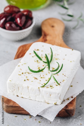 Homemade greek cheese feta with rosemary and herbs on cutting board with olive oil and olives