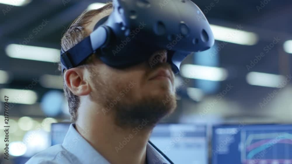 Close-up Portrait of the Industrial Engineer Putting on Virtual Reality Headset, ready to Work. In the Background Manufacturing Plant and Monitors. Close-up Portrait of the Industrial Engineer Putting on Virtual Reality Headset, ready to Work. In the Background Manufacturing Plant and Monitors.