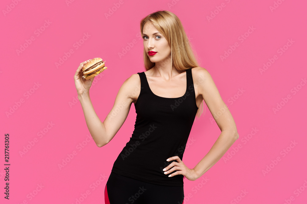 Beautiful girl on a pink background holds a burger. The concept of an unhealthy diet Beautiful girl on a pink background holds a burger. The concept of an unhealthy diet