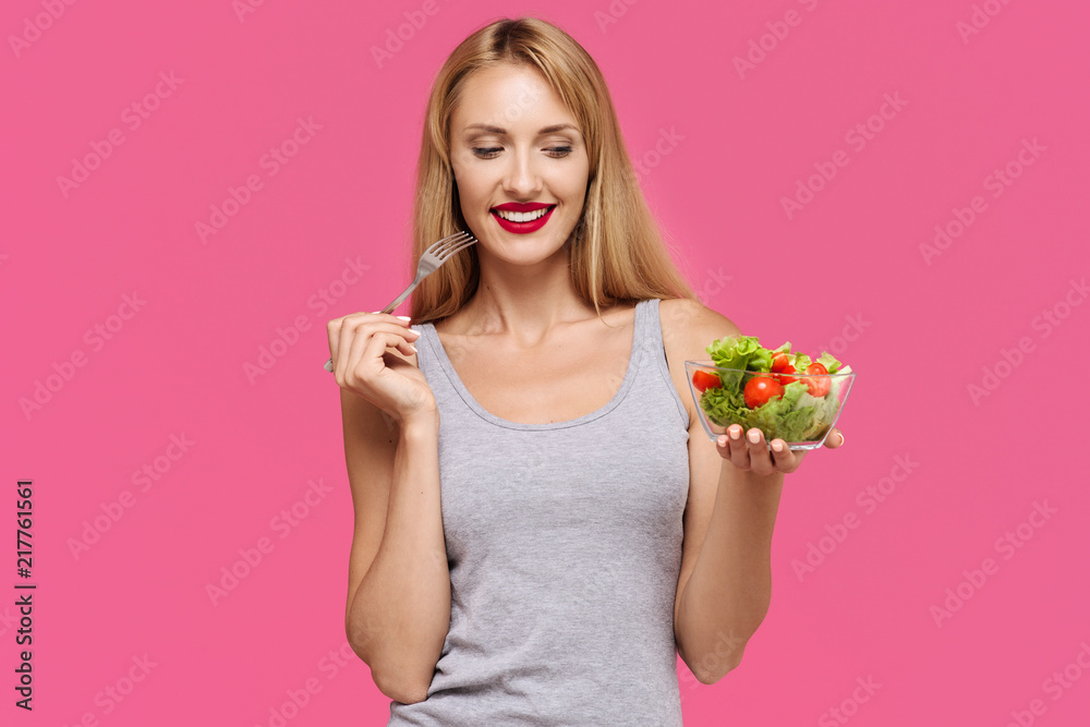Young beautiful girl with on a pink background holds vegetable salad and fork in hands. Concept of healthy food Young beautiful girl with on a pink background holds vegetable salad and fork in hands. Concept of healthy food