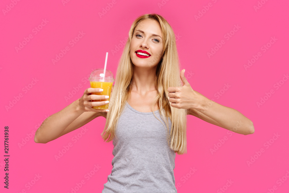 Young beautiful slender girl with a pink background holding orange juice smiling and showing thumb up. Concept of un healthy fat junk and healthy food Young beautiful slender girl with a pink background holding orange juice smiling and showing thumb up. Concept of un healthy fat junk and healthy food