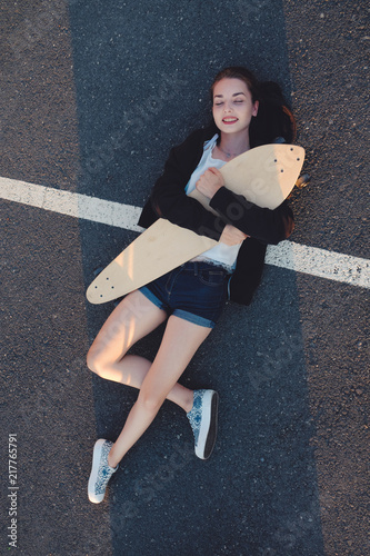 Skateg girl lying down with her longboard on asphalt street surface