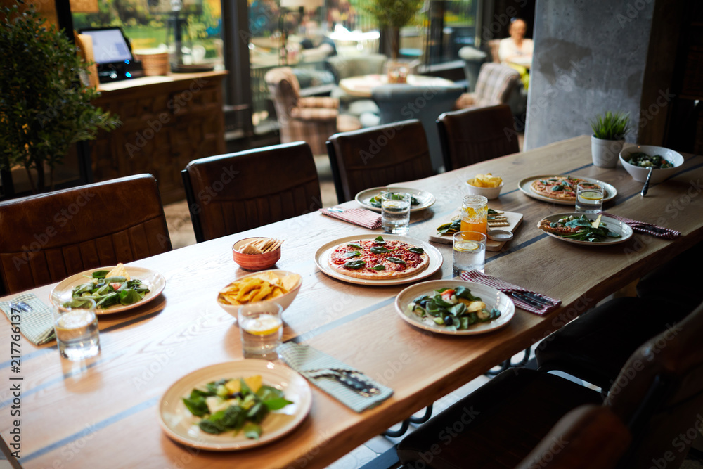 Wooden table in cafe or restaurant served with salad, pizza and other snack for guests