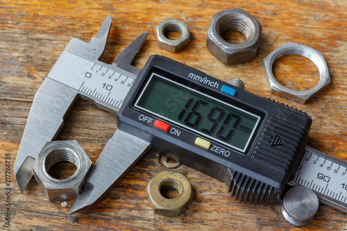 Digital electronic caliper with used nuts on wooden table in workshop