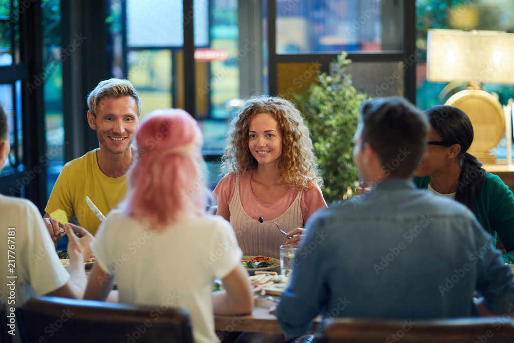 Happy guy and girl looking at their friends by served table during talk in cafe or restaurant Happy guy and girl looking at their friends by served table during talk in cafe or restaurant