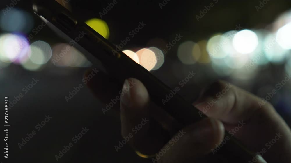 Close up man hands using smartphone at night on illumination bokeh color light in night atmospheric city street background. Male hand with mobile phone searching, typing and social networks concepts. 