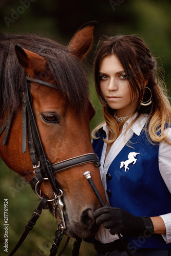 Young woman equestrian rider stands brown horse in forest. Concept friends