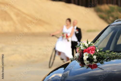 Bukiet ślubny na samochodzie, młoda para na rowerze.