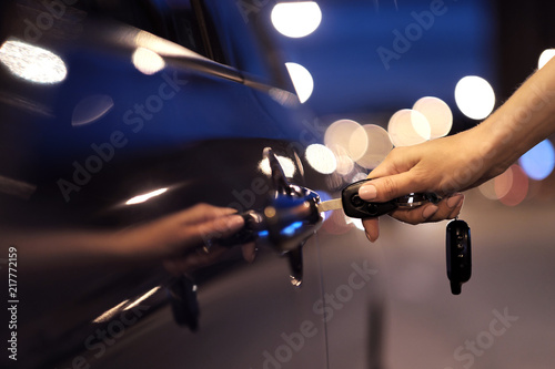 Close-up of a female hand pressing a button on a key ring of car keys, against the background of a car door.