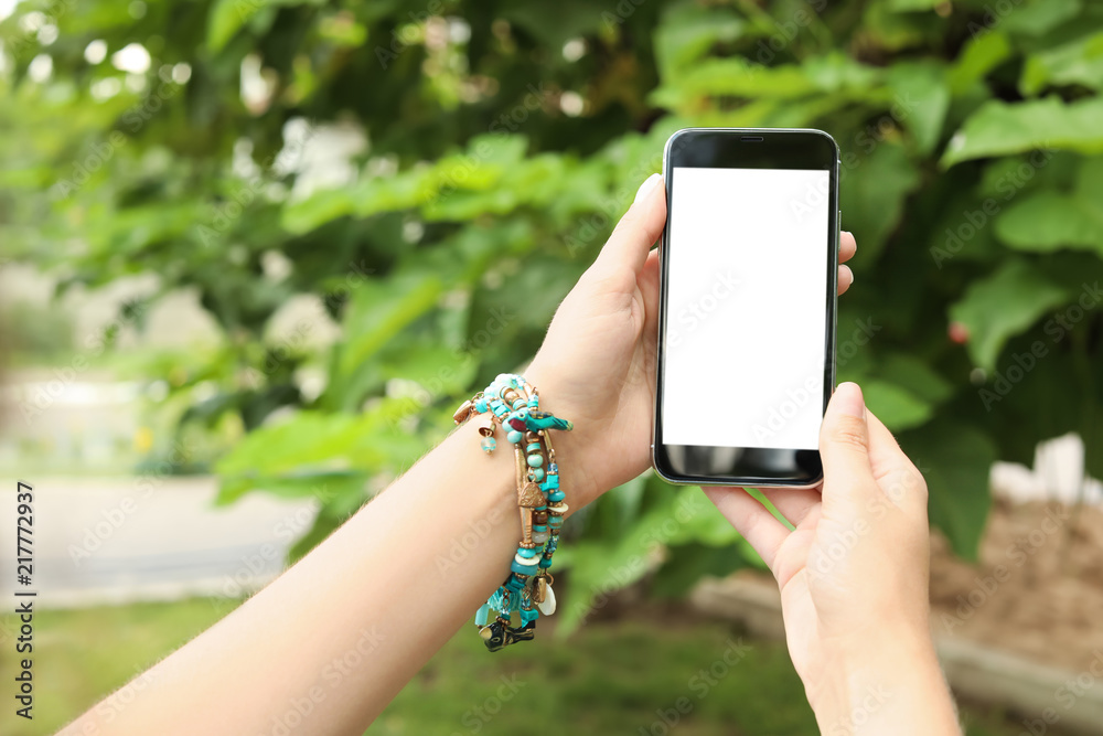 Woman holding smartphone with blank screen outdoors. Mockup for design