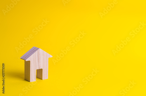 A small wooden house stands on a yellow background. The concept of buying and selling real estate, renting. Search for a house. Affordable housing, credit and loans. Investments in business