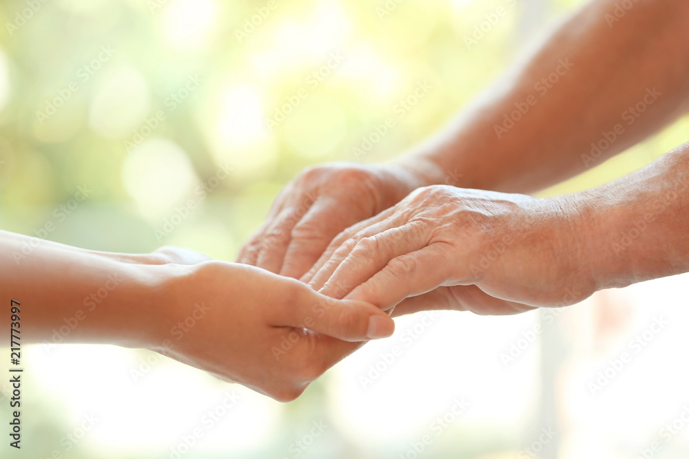 Young woman holding elderly man hands on blurred background, closeup. Help service Young woman holding elderly man hands on blurred background, closeup. Help service