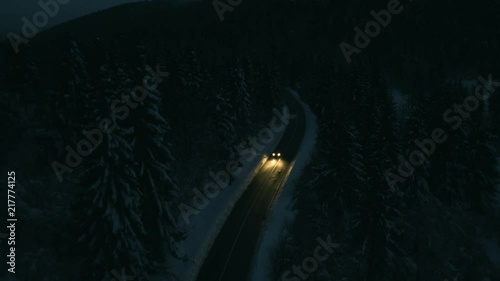 Aerial shot of a car driving through an icy spruce forest at night. photo