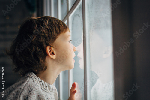 Little boy waiting for Santa Clause. Cute curly toddler boy sitting near the window