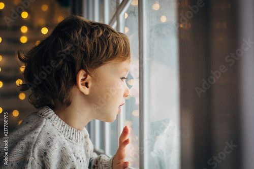 Little boy waiting for Santa Clause. Cute curly toddler boy sitting near the window